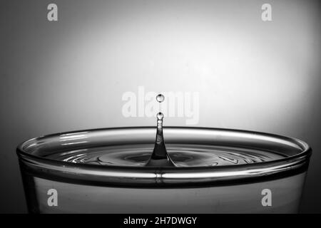 Prise de vue en niveaux de gris d'eau tombant dans une vitre sur un fond gris Banque D'Images