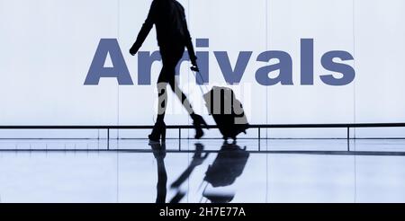 Femme avec bagages à roulettes/valises devant le panneau des arrivées dans le terminal de l'aéroport. Banque D'Images