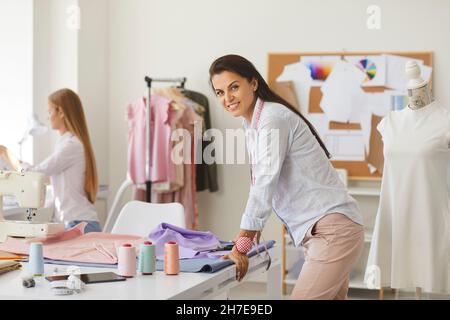 Portrait d'une jeune femme heureuse qui travaille comme couturière debout à table et souriante Banque D'Images