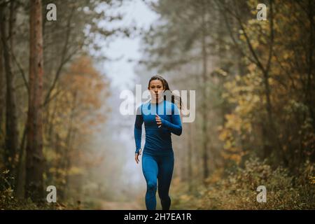 Jeune femme en costume bleu de course vers la caméra sur le sentier forestier à l'automne Banque D'Images