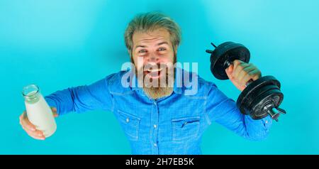 Homme barbu souriant avec lait et haltères.Produits laitiers.Cocktail de protéines.Vitamines pour les muscles. Banque D'Images