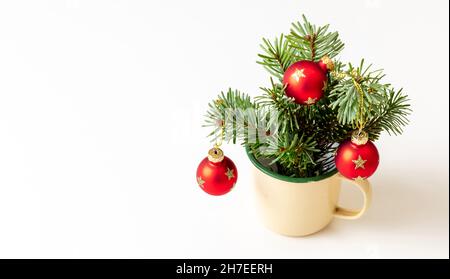 Brindilles de sapin frais de Noël et boules rouges dans une tasse de café en émail isolée sur fond blanc, carte de vœux du nouvel an Joyeux de Noël Banque D'Images