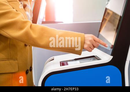 Les passagers de type femme utilisent un kiosque en libre-service avec écran tactile pour s'enregistrer au vol afin d'éviter les longues files d'attente dans la vue latérale du terminal d'aéroport contemporain Banque D'Images
