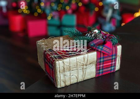 Magnifique boîte cadeau de noël enveloppée de papier artisanal et attachée avec un ruban à carreaux décoré d'une branche d'épicéa.Cadeau fait maison.Des lumières de noël défocacées et un arrière-plan de présentation. Banque D'Images
