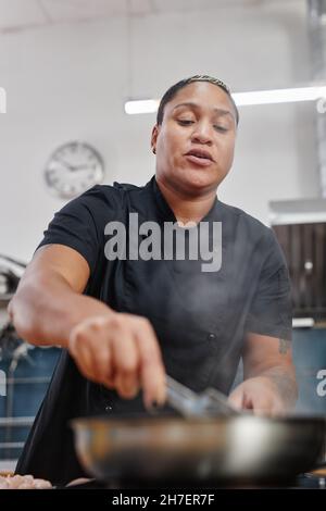 Portrait à angle bas d'une femme de chef latino-américaine qui friture de la viande tout en cuisinant dans une cuisine professionnelle Banque D'Images