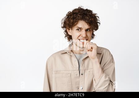 Garçon anxieux avec les cheveux bouclés doigt, regardant peur et inquiet, pensant à quelque chose de problématique, fond blanc Banque D'Images