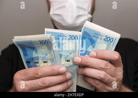 Finance pendant le coronavirus en Israël concept.Nouveaux billets de shekels israéliens avec le nouveau NIS 200. l'homme d'âge moyen dans le masque médical de protection du visage pays Banque D'Images