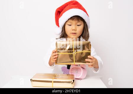Petite fille asiatique en chapeau de père noël assis avec des boîtes-cadeaux isolées sur fond blanc. Banque D'Images