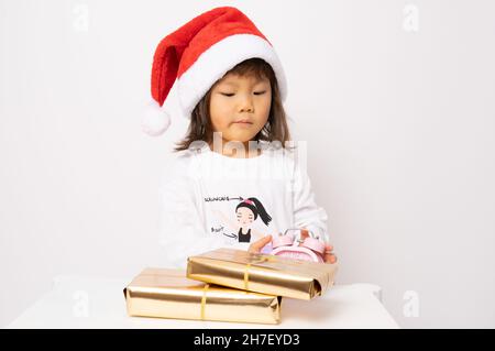 Petite fille asiatique en chapeau de père noël assis avec des boîtes-cadeaux isolées sur fond blanc. Banque D'Images