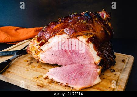 Jambon glacé orange Bourbon sur une planche à découper en bambou : jambon glacé en os tranché sur une planche à découper en bois Banque D'Images