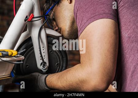 Mécanicien installant la roue neuve ou réparée sur un scooter électrique dans son atelier Banque D'Images