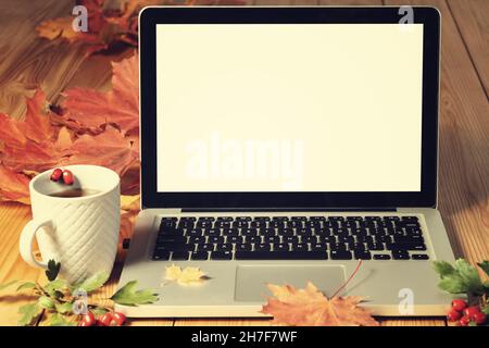 Ordinateur portable ouvert avec écran vierge sur table en bois avec feuilles d'automne et mug Banque D'Images