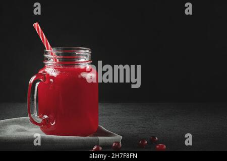 Curatif jus de canneberge dans un pot-mug en verre avec une paille sur table noire. Concept de saine alimentation avec espace de copie Banque D'Images