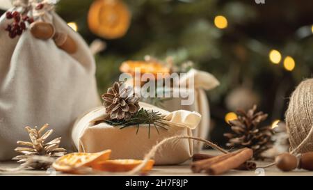 Concept de noël zéro déchet. Emballé dans des cadeaux et des décorations en tissu naturel à partir de matériaux naturels sur une table en bois près de l'arbre de Noël avec des lumières. Banque D'Images