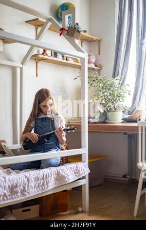 Focalisé petite fille jouant la mélodie sur ukulele pratiquant l'exercice musical appréciant l'étude éducative Banque D'Images