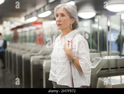 Femme européenne mûre debout près des barrières tarifaires dans la station de métro. Banque D'Images