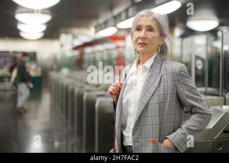 Femme européenne mûre debout près des barrières tarifaires dans la station de métro. Banque D'Images