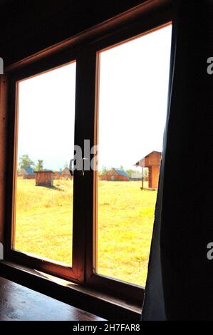 Une vue à travers la fenêtre de la chambre à un pré ensoleillé avec d'autres maisons.Altaï, Sibérie, Russie . Banque D'Images