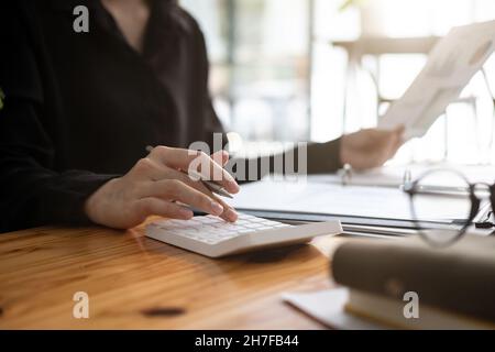 Gros plan femme d'affaires travaillant avec la calculatrice pour document financier dans le bureau. Homme comptable faisant la comptabilité et le calcul. Livre comptable Banque D'Images