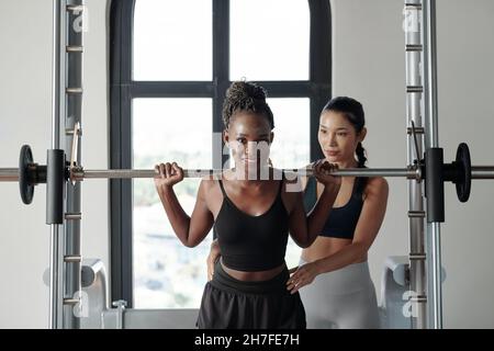 Entraîneur de forme physique contrôlant la posture de la cliente femelle se préparer à faire des squats avec le barbell lourd Banque D'Images