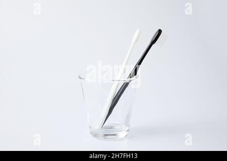 brosses à dents blanches noires dans des articles de toilette en verre isolés sur fond blanc Banque D'Images