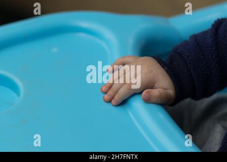 Un gros plan d'une main d'un bébé sale mangeant de la nourriture, sur une chaise de bébé bleue Banque D'Images