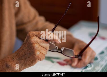 Un gros plan des mains d'une femme âgée tenant une paire de lunettes MR - modèle libéré Banque D'Images