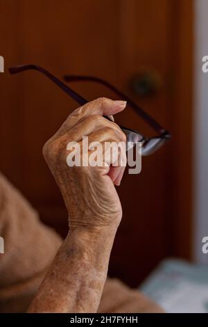 Un gros plan des mains d'une femme âgée tenant une paire de lunettes MR - modèle libéré Banque D'Images