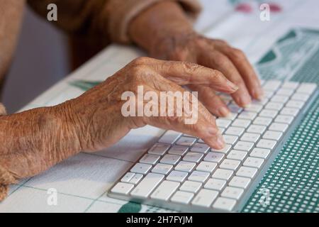 Un gros plan des mains d'une femme âgée taper sur un clavier sans fil MR - modèle libéré Banque D'Images