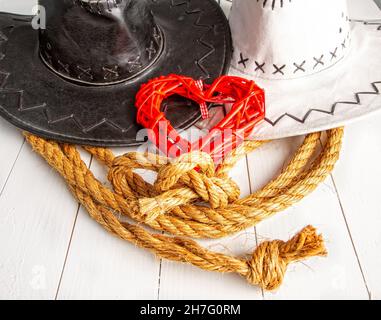 Image conceptuelle d'un mariage rural de cow-boys.Chapeau de mariée blanc et chapeau de marié foncé et coeur rouge symbole de l'amour Banque D'Images