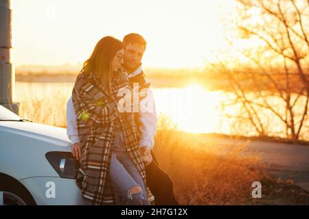 Le voyageur de couple se tient en voiture au coucher du soleil dans la campagne.Elle utilise la carte des applications mobiles dans son smartphone pour trouver le chemin.Les touristes qui vérifient la position dans la carte du smartphone.Mise au point douce Banque D'Images