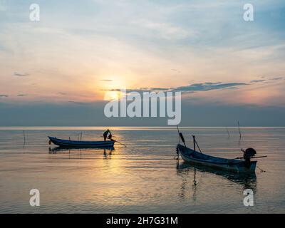 Homme préparant son bateau à l'aube sur la côte de la province de Surat Thani en Thaïlande. Banque D'Images