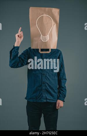 Jeune homme avec un sac en papier sur sa tête, ampoule, ayant une idée, démarrer Banque D'Images