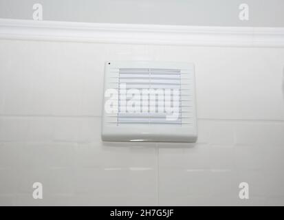 Un gros plan d'un ventilateur de salle de bains, ventilateur d'évacuation, ventilation de salle de bains avec barbecue blanc installé sur un mur de carrelage blanc. Banque D'Images