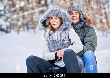 Couple s'amusant avec un traîneau sur la neige en hiver Banque D'Images