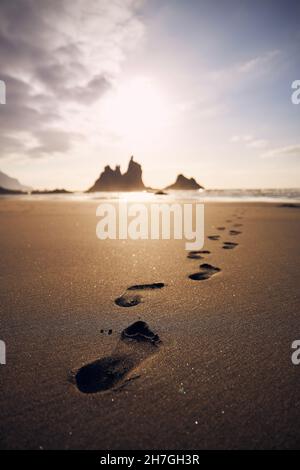 Empreintes de pieds dans le sable sur la plage menant à la mer.Coucher de soleil doré à Ténérife, îles Canaries, Espagne. Banque D'Images