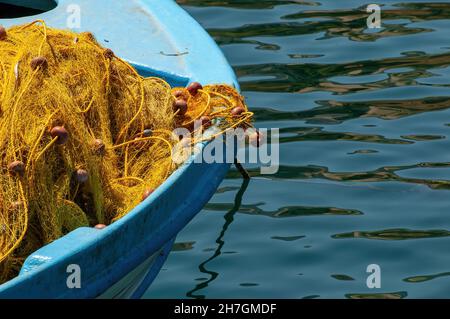 Vue rapprochée de l'avant d'un bateau de pêche bleu amarré en bois avec filets de pêche en nylon jaune avec corde et flotteurs drapés sur l'avant du bateau Banque D'Images
