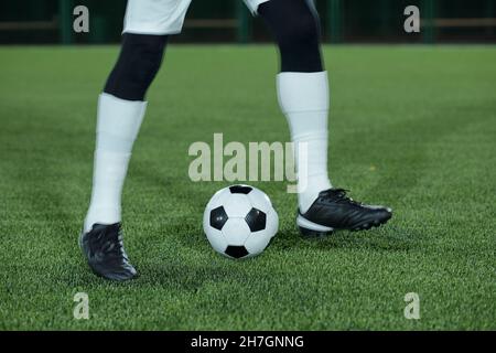 Jambes de joueur de football en chaussettes blanches et chaussures de sport noires s'exerçant avec le ballon de football sur la pelouse verte au stade Banque D'Images