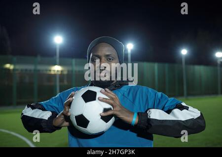 Jeune homme africain en uniforme sportif tenant le ballon de football devant lui tout en pratiquant l'exercice pendant l'entraînement Banque D'Images