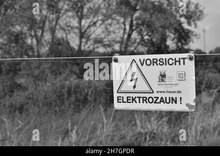 BRAUNSCHWEIG, ALLEMAGNE - 13 octobre 2021 : photo en niveaux de gris d'un panneau d'avertissement sur une clôture d'un pâturage. Banque D'Images