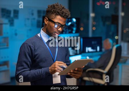 Jeune programmeur africain de sexe masculin défilant dans le pavé tactile tout en regardant à travers de nouveaux logiciels informatiques dans l'Internet Banque D'Images