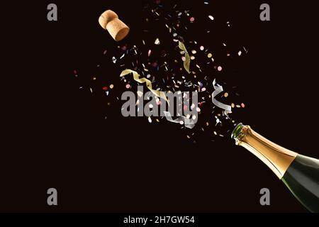 Concept festif avec une bouteille de vin mousseux fraîchement ouverte, confettis et rubans sortis sur fond noir isolé Banque D'Images