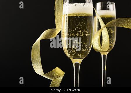 Détail de deux verres de vin blanc mousseux et noeud doré avec fond noir isolé.Vue avant. Banque D'Images