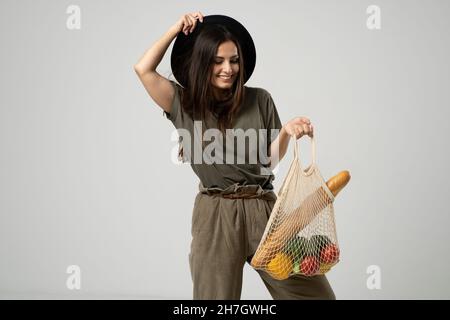 Une femme moderne et élégante avec un sac de shopping en filet avec des légumes sur le fond du studio.Le concept de nutrition saine, végétarisme Banque D'Images