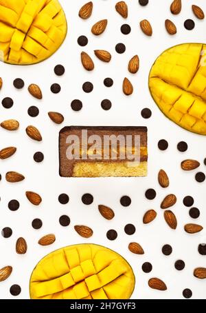 Vue de dessus d'une délicieuse tranche de gâteau de mousse au chocolat à la mangue avec les couches affichées et les ingrédients de la recette disposés sur fond blanc.Menu du restaurant et concept de confiserie en pose plate. Banque D'Images