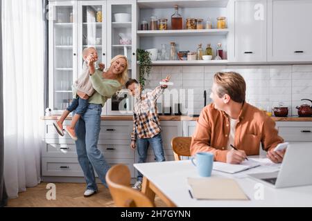 femme gaie s'amusant avec des fils près de brouillé mari travaillant dans la cuisine Banque D'Images