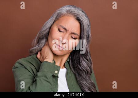 Photo de triste aîné blanc coiffure dame main cou porter chemise isolée sur fond brun couleur Banque D'Images