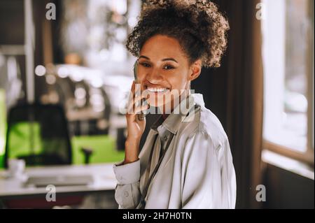 Mignonne à la peau sombre et souriante, elle parle au téléphone Banque D'Images