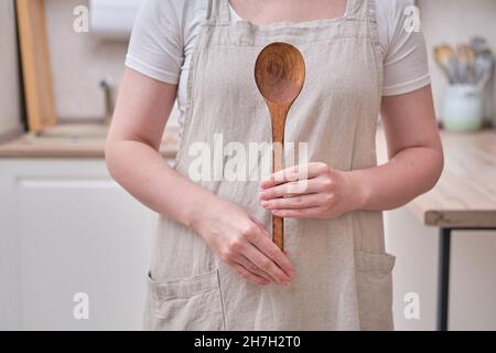Une grande cuillère en bois dans les mains d'une femme dans la cuisine.Les mains des femmes tiennent une cuillère à salade Banque D'Images
