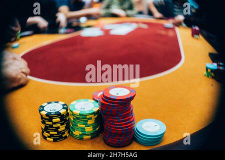 Gros plan de jetons de poker sur la table avec des personnes jouant au Texas Hold 'EM, en arrière-plan Banque D'Images